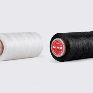 May include: Two spools of thread, one white and one black, are displayed side-by-side. Each spool has a red and white label with the word "GALACES" printed on it. The thread is tightly wound around a cardboard core.