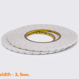 Op de afbeelding: Twee rollen dubbelzijdige plakband. Het tape is wit met een gestippeld patroon langs de randen. De binnenkern is geel met zwarte tekst. De breedte is 3,5 mm.