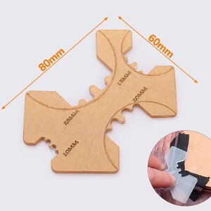 May include: A tan-colored zipper guide tool with measurements in millimeters. The tool is 80mm long and 60mm wide, with cutouts for 10mm, 18mm, 20mm, and 25mm zippers. A small inset shows the tool in use.