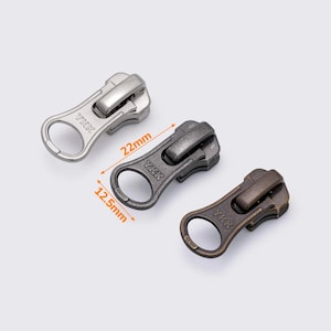 以下が含まれることがあります： シルバー、ガンメタル、ブロンズの3色の金属製ファスナー引き手。ガンメタルの引き手は長さ2.2cm、幅1.25cmです。各引き手にはリングとYKKのブランド名が付いています。