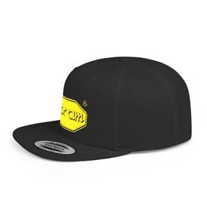 Könnte beinhalten: Schwarze Cap mit flachem Schirm und gelbem Vibram-Logo. Das Logo ist ein gelbes Sechseck mit dem Wort "Vibram" in Gelb. Die Cap hat einen Snapback-Verschluss und einen flachen Schirm.