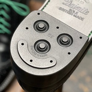 K&ouml;nnte beinhalten: Nahaufnahme der Sohle eines schwarzen Lederschuhs mit einer schwarzen Gummisohle. Die Sohle hat ein strukturiertes Muster und die Worte "Dainite Sole British Made" sind auf der Ferse aufgedruckt.