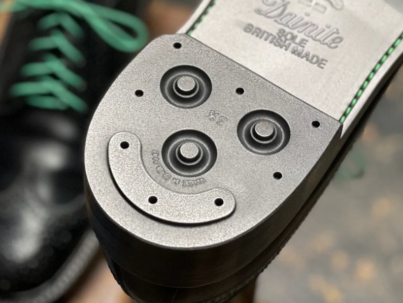 K&ouml;nnte beinhalten: Nahaufnahme der Sohle eines schwarzen Lederschuhs mit einer schwarzen Gummisohle. Die Sohle hat ein strukturiertes Muster und die Worte "Dainite Sole British Made" sind auf der Ferse aufgedruckt.