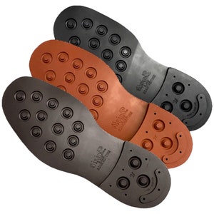 Op de afbeelding: Drie schoenzool in verschillende kleuren: zwart, bruin en oranje. Elke zool heeft een patroon van kleine cirkels en een gebogen ontwerp op de hiel. De zolen zijn gemarkeerd met "Vibram" en "Made in Italy".