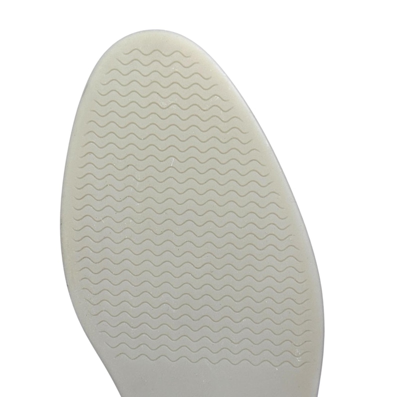 May include: Close-up of a shoe sole in a light beige hue. The sole has a rounded form and a textured surface featuring a wavy pattern. The design is consistent across the entire sole, offering grip and support.