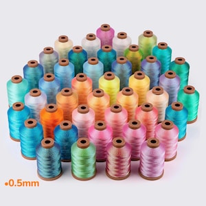 May include: A collection of colorful embroidery thread spools in various shades, including teal, orange, pink, and green. The spools are arranged closely together, with the text ".0.5mm" in the lower left corner.