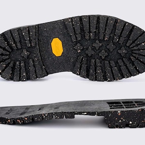 Peut inclure: Gros plan sur la semelle d'une botte noire avec une semelle texturée. La semelle a un motif de bande de roulement jaune et une petite étiquette jaune avec le mot "Vibram" imprimé dessus.