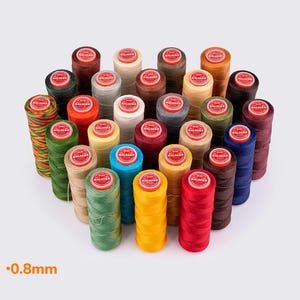 Könnte beinhalten: Eine Sammlung bunter Garnrollen, jede mit einem roten Etikett. Die Fäden sind in verschiedenen Farben erhältlich, darunter Rot, Gelb, Grün, Blau und Braun. Der Text "-0,8 mm" ist unten links sichtbar.