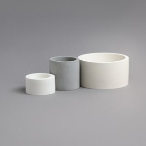 May include: Three cylindrical containers, one gray and two white, arranged in a row from smallest to largest.