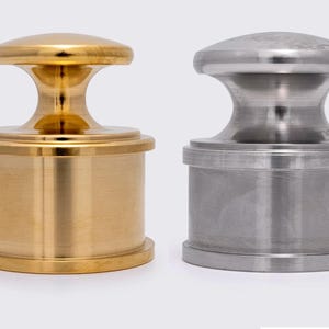 May include: Two metal objects with a cylindrical base and a rounded top. One is gold-colored, the other is silver. The objects have a classic, symmetrical design, suitable for decorative or functional use.