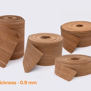 May include: Four rolls of brown corrugated paper ribbon, each with a thickness of 0.9 mm. The rolls vary in size, with some partially unrolled, revealing the ribbed texture. The text "thickness - 0.9 mm" is displayed in orange.