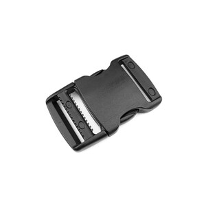 Può includere: Fibbia laterale in plastica nera, progettata per fissare cinghie. La fibbia presenta un'estremità maschio e femmina, con un meccanismo dentato per un fissaggio sicuro. L'immagine è un primo piano su sfondo bianco.