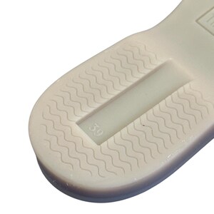 May include: Close-up of a shoe sole with a wavy pattern and a recessed area. The number "39" is visible in the recessed area. The sole is off-white.