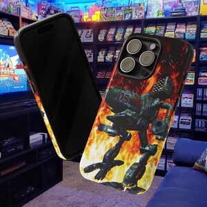 May include: Black smartphone case with a green and black robot design set against a fiery orange and yellow background. The case is shown with a black smartphone, showcasing the design and the phone's camera.
