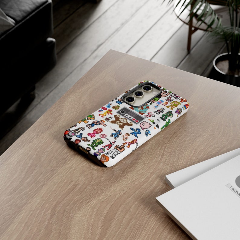 May include: A white phone case with a pixelated design of video game characters. The case has a black camera lens and a black outline around the design.