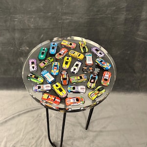 May include: A round clear table with a black metal base. The table top is filled with colorful toy cars.