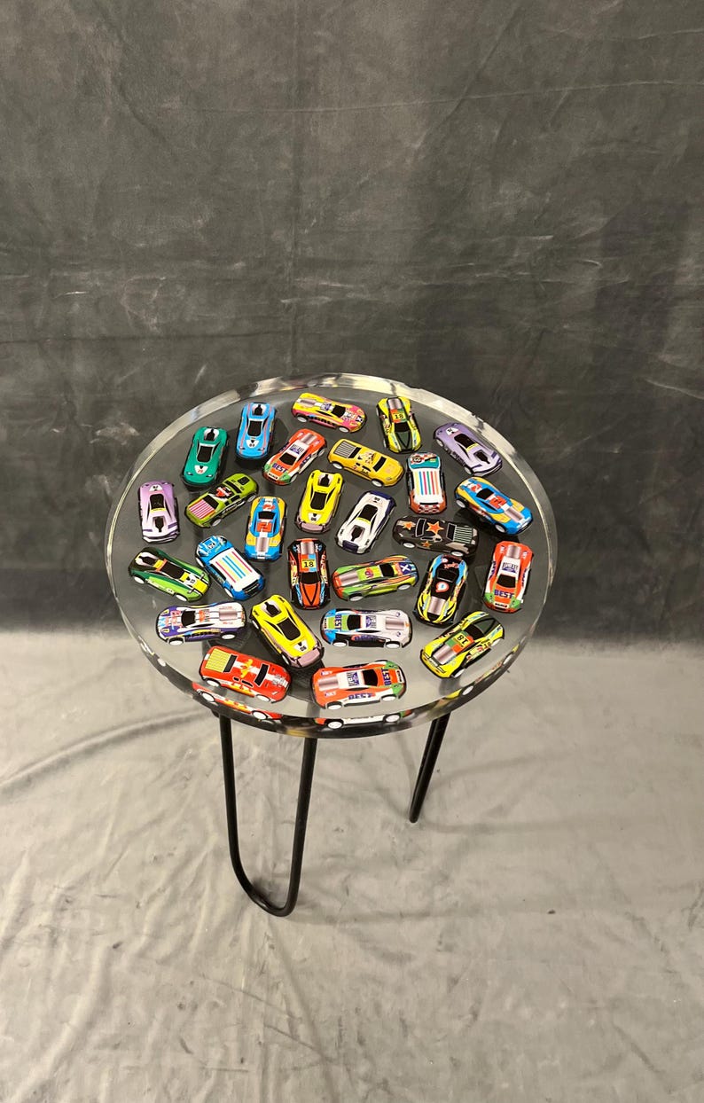 May include: A round clear table with a black metal base. The table top is filled with colorful toy cars.