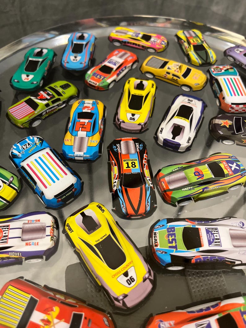 May include: A collection of colorful toy race cars with various designs and numbers. The cars are made of plastic and have a variety of colors, including red, blue, green, yellow, and black. The cars are all different sizes and shapes, and some have different designs on them. The cars are all on a clear surface.