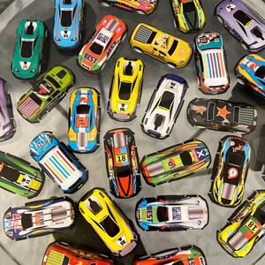 May include: A collection of colorful toy race cars with various numbers and designs. The cars are made of metal and have a pull-back and go action.