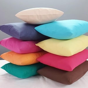 Peut inclure: Une pile de huit oreillers de différentes couleurs, dont blanc, violet, bleu, jaune, orange, rose, sarcelle et marron. Les oreillers sont disposés en forme de pyramide, avec l'oreiller blanc en haut.