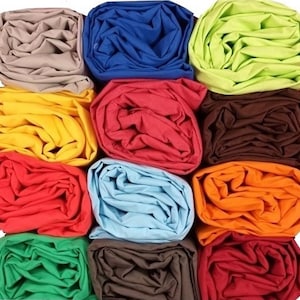 Peut inclure: Une grille de tissus roulés de différentes couleurs : beige, bleu, jaune, rouge, marron, bleu clair, orange, vert et bordeaux. Le tissu semble être une matière douce, peut-être du coton ou du lin.