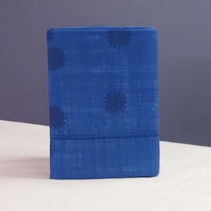 Könnte beinhalten: Ein gefalteter, rechteckiger blauer Stoff mit einem Blumenmuster. Der Stoff hat einen leuchtenden Blauton, mit dunkleren blauen Blumendesigns, die gleichmäßig über die Oberfläche verteilt sind. Der Stoff scheint aus Baumwolle oder einem ähnlichen Material zu sein.