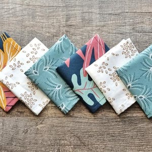 May include: A collection of six square fabric napkins with various colorful floral and leaf patterns. The napkins are arranged on a wooden surface, showcasing a range of colors including pink, blue, white, and navy.