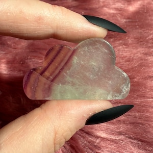 May include: A cloud-shaped piece of fluorite crystal with purple and green stripes. The crystal is translucent and has a smooth, polished surface.