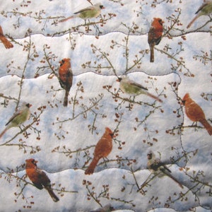 May include: A white fabric with a repeating pattern of red cardinals and small brown branches on a white background.