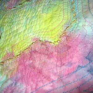 May include: A close-up of a colorful fabric with a quilted texture. The fabric is a blend of pink, blue, green, and yellow hues. The fabric is decorated with gold thread embroidery in a swirling pattern.