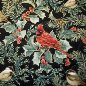 May include: A quilted fabric featuring a repeating pattern of birds, holly leaves, red berries, and pine needles on a black background. The birds include a vibrant red cardinal and smaller tan and white birds. Gold accents highlight the details.