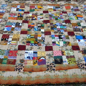 May include: A patchwork quilt with a beige background and a grid of colorful squares. The squares are made of different fabrics with various patterns and colors, including red, blue, green, yellow, and brown.