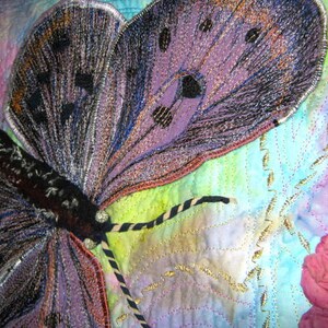 May include: A close-up of a purple and black butterfly embroidered on a fabric background. The butterfly has intricate details and is surrounded by a light blue and green watercolor wash.