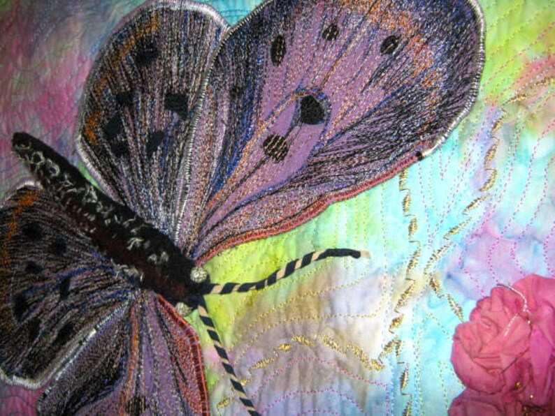 May include: A close-up of a purple and black butterfly embroidered on a fabric background. The butterfly has intricate details and is surrounded by a light blue and green watercolor wash.