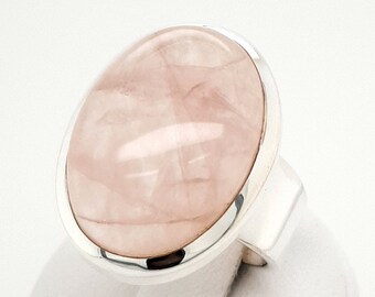 May include: A silver ring with a large oval-shaped pink rose quartz gemstone.