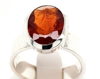 May include: A silver ring with an oval-shaped orange gemstone set in a bezel setting.