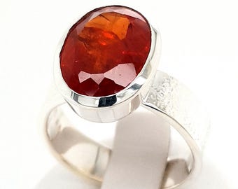 May include: A silver ring with an oval-shaped, faceted, orange gemstone set in a bezel setting.