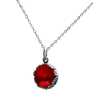 May include: A silver necklace with a round, red pendant. The pendant is encased in a decorative silver frame with leaf-like details. The chain is a delicate, linked design.