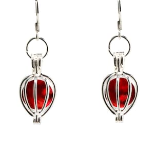 May include: A pair of silver earrings with red glass orbs inside a cage-like design.
