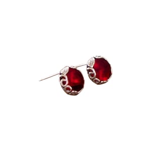 May include: A pair of silver stud earrings with red gemstone accents. The earrings feature a delicate leaf design around the gemstones.