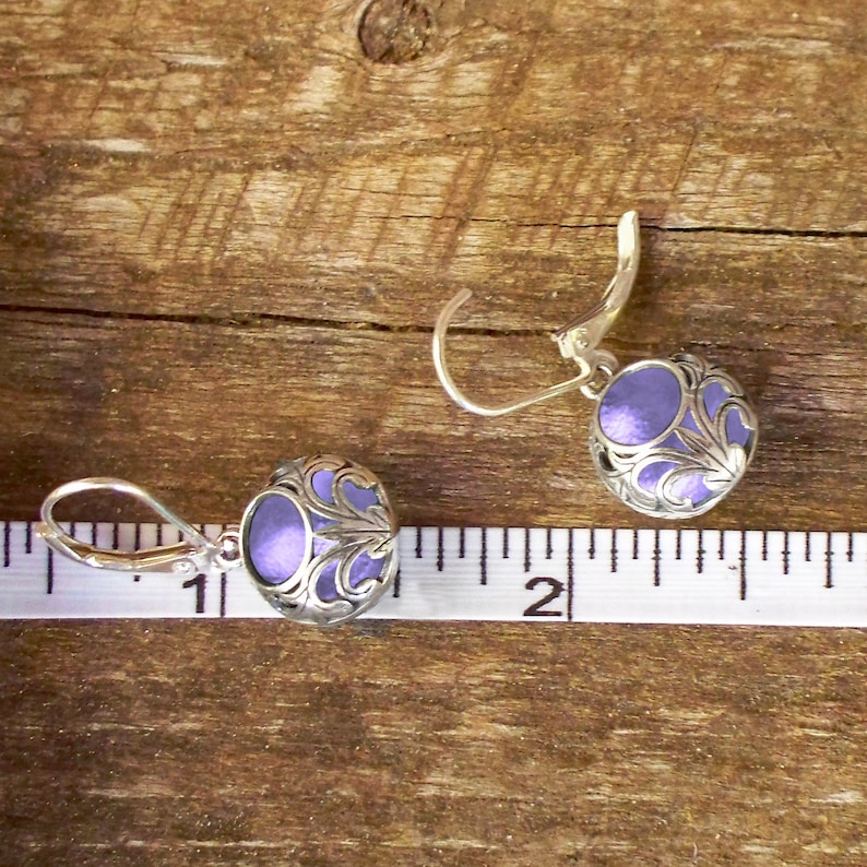 May include: A pair of silver dangle earrings with a purple, filigree design. The earrings are approximately 1 inch long.