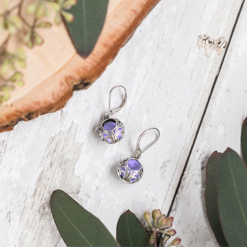 May include: A pair of silver earrings with purple glass stones set in a filigree design.