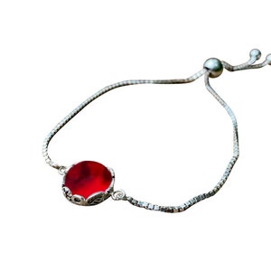 May include: A silver chain bracelet with a red gemstone pendant. The bracelet has an adjustable sliding clasp.