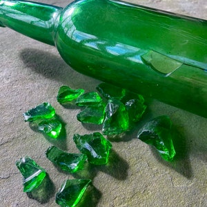 Op de afbeelding: Een gebroken groene glazen fles met scherven glas verspreid eromheen op een grijs oppervlak.