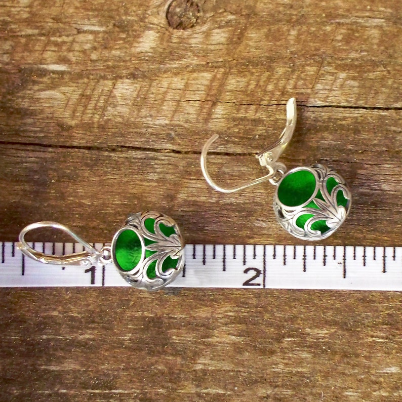 Op de afbeelding: Een paar zilveren oorhangers met groene glazen cabochons. De oorhangers zijn ongeveer 2,5 cm lang.