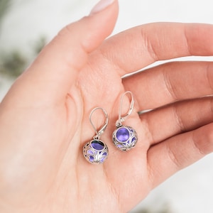 May include: A pair of silver earrings with a purple stone set in a filigree design.