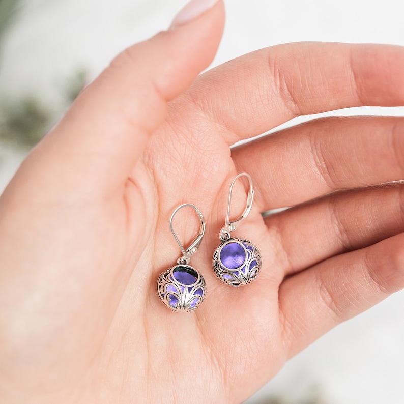 May include: A pair of silver earrings with a purple stone set in a filigree design.