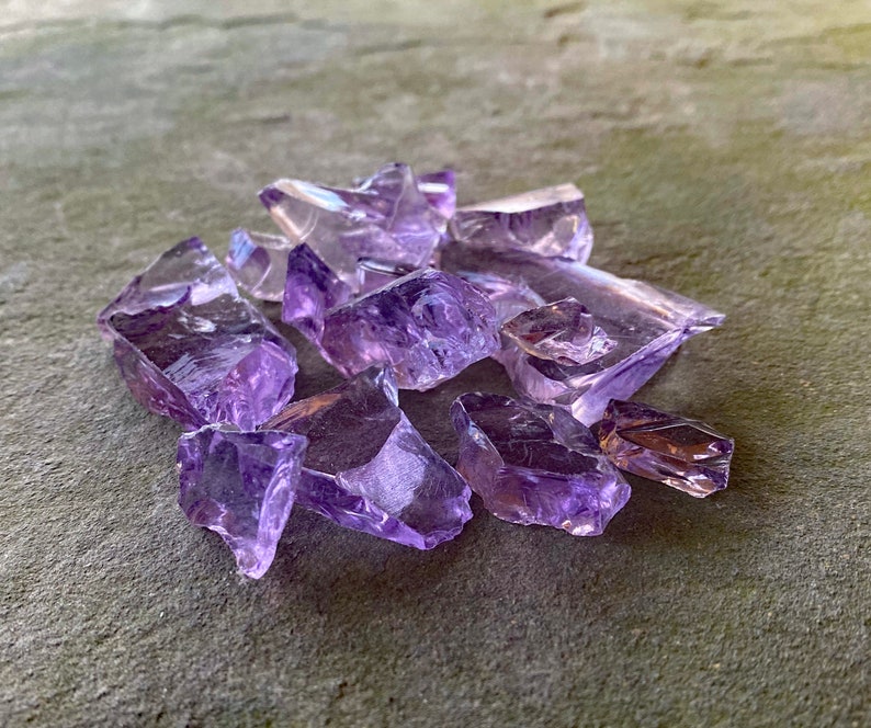 May include: A collection of amethyst crystal chips in various sizes and shapes. The chips are a light purple colour and have a translucent appearance.
