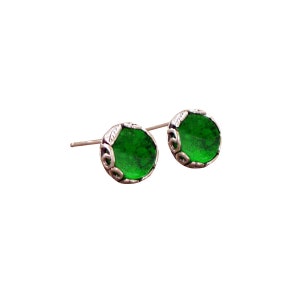 May include: A pair of silver stud earrings with green glass stones set in a decorative silver frame.