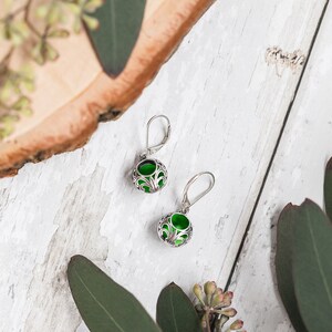 Op de afbeelding: Een paar zilveren oorbellen met groene glazen cabochons, ingelegd in een ingewikkeld filigraanontwerp.